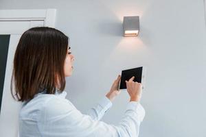 Switching the lighting. Young woman is indoors in smart house room at daytime photo