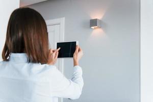 cambiar la iluminación. la mujer joven está adentro en la habitación de la casa inteligente durante el día foto