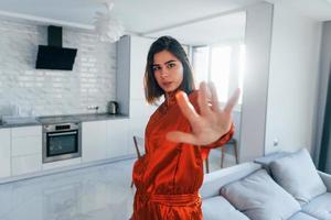 Posing for a camera in red costume. Young woman is indoors in room of modern house at daytime photo