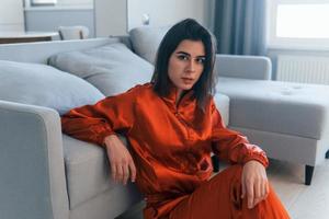 Posing for a camera in red costume. Young woman is indoors in room of modern house at daytime photo