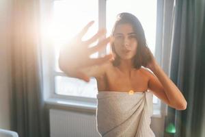 In white towel. Young woman is indoors in room of modern house at daytime photo