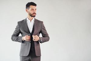 Posing for a camera against white background. Young stylish businessman in suit indoors photo