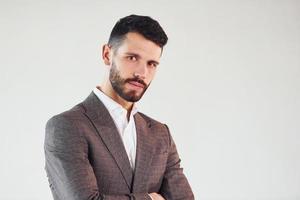 Posing for a camera against white background. Young stylish businessman in suit indoors photo