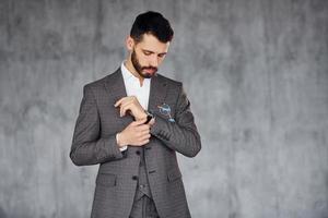 de pie contra el fondo gris. joven y elegante hombre de negocios con traje en el interior. concepción del éxito foto