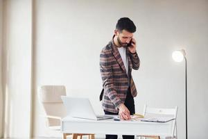 Works in the office. Young stylish businessman in suit indoors. Conception of success photo