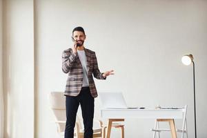 tener una conversación por teléfono. joven y elegante hombre de negocios con traje en el interior. concepción del éxito foto