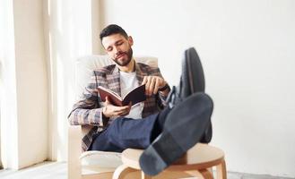 Reads book. Young stylish businessman in suit indoors. Conception of success photo