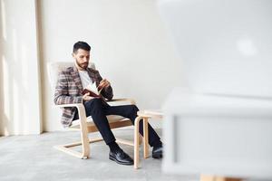 Reads book. Young stylish businessman in suit indoors. Conception of success photo