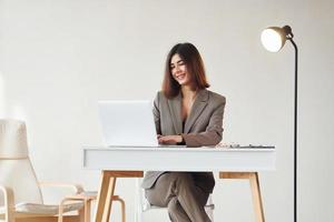 Works in the office by laptop. Young woman in formal clothes is indoors. Conception of style photo