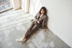 Sits on the floor. Young woman in formal clothes is indoors. Conception of style photo