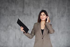 Talks by phone. Young woman in formal clothes is indoors. Conception of style photo