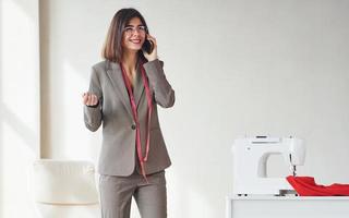 Seamstress talks by phone. Young woman in formal clothes is indoors. Conception of style photo