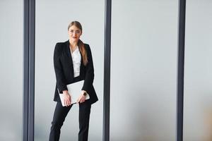 Standing against grey background. Young adult woman in formal clothes is indoors in the office photo