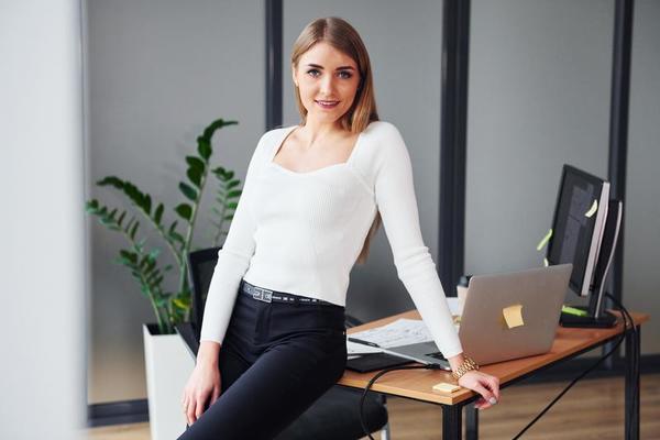 Young adult woman in formal clothes is indoors against grey