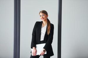 With laptop. Young adult woman in formal clothes is indoors in the office photo