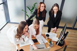 Working by table with laptop. Group of adult women that in formal clothes is indoors in the office together photo