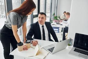 Works by using laptop. Group of people in official formal clothes that is indoors in the office photo