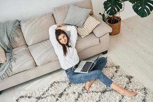 With laptop. Beautiful young woman in jeans and white shirt is at home photo