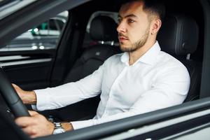 Successful man. Young guy in white shirt is sitting inside of a modern new automobile photo