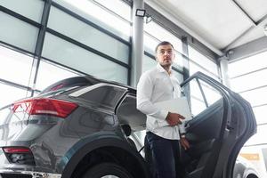 Young man in white shirt is indoors with modern new automobile photo