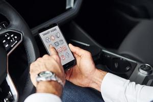 se sienta en el coche. vista de cerca de la mano del hombre que sostiene el teléfono con etiquetas e íconos. concepto de control remoto foto