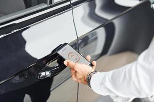 coche negro. vista de cerca de la mano del hombre que sostiene el teléfono con etiquetas e íconos. concepto de control remoto foto