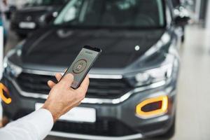 coche negro. vista de cerca de la mano del hombre que sostiene el teléfono con etiquetas e íconos. concepto de control remoto foto