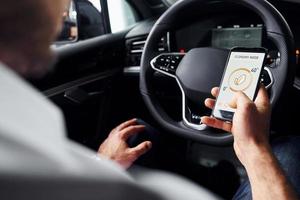 Sits in the car. Close up view of man's hand that holds phone with labels and icons. Conception of remote control photo