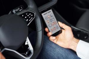 Sits in the car. Close up view of man's hand that holds phone with labels and icons. Conception of remote control photo