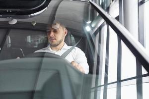 Young man in white shirt is sitting inside of a modern new automobile photo