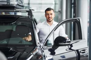 Young man in white shirt is indoors with modern new automobile photo