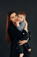 madre con ropa negra elegante está con su pequeño hijo en el estudio foto