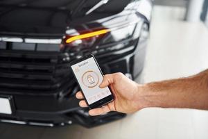 Black car. Close up view of man's hand that holds phone with labels and icons. Conception of remote control photo