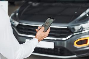 Black car. Close up view of man's hand that holds phone with labels and icons. Conception of remote control photo