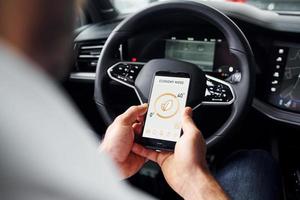 se sienta en el coche. vista de cerca de la mano del hombre que sostiene el teléfono con etiquetas e íconos. concepto de control remoto foto