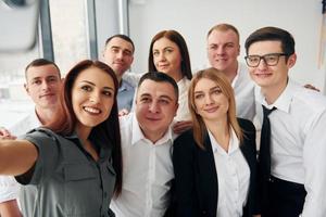 Makes selfie. Group of people in official formal clothes that is indoors in the office photo