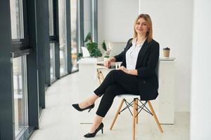 Woman in formal clothes is sitting on the chair indoors in the modern office at daytime photo