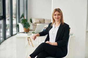 Woman in formal clothes is sitting on the chair indoors in the modern office at daytime photo