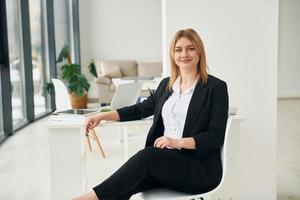 mujer con ropa formal está sentada en la silla en el interior de la oficina moderna durante el día foto