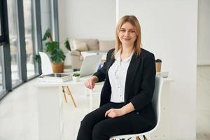 Woman in formal clothes is sitting on the chair indoors in the modern office at daytime photo