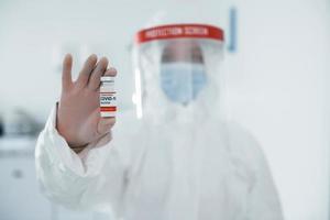 Holds test tube. Female medical worker in protective uniform works on COVID-19 vaccine photo