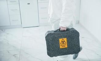 Holds case with biological hazard. Female medical worker in protective uniform works on COVID-19 vaccine photo