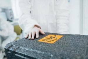 Holds case with biological hazard. Female medical worker in protective uniform works on COVID-19 vaccine photo