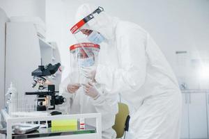 Using microscope. Female medical workers in protective uniform works on COVID-19 vaccine photo