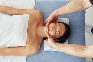 Top view. Young woman is lying down when man doing massage of her body at spa photo