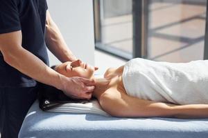 Room illuminated by sun beams. Young woman is lying down when man doing massage of her body at spa photo