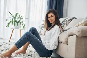 hermosa joven en jeans y camisa blanca está en casa foto