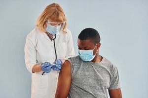 Senior doctor giving injection to young african american man at hospital photo