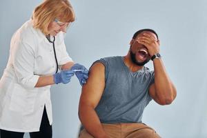 Senior doctor giving injection to young african american man at hospital photo