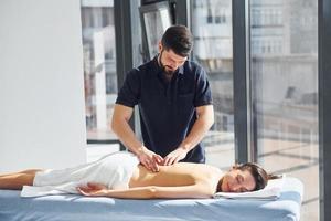 Room illuminated by sun beams. Young woman is lying down when man doing massage of her body at spa photo